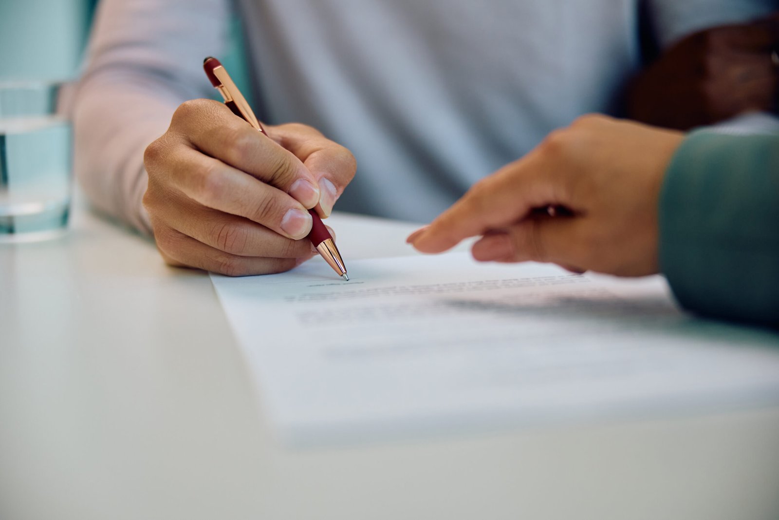 Close up of man signing contract while having a meeting with real estate agent in the office.